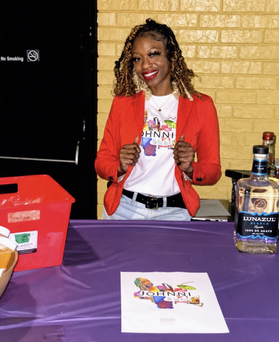 Johnni smiling in a red blazer at a branded event bar